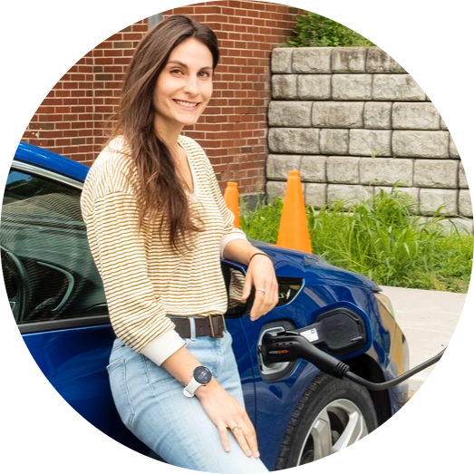 苏Fassler leaning against a blue electric car being charged